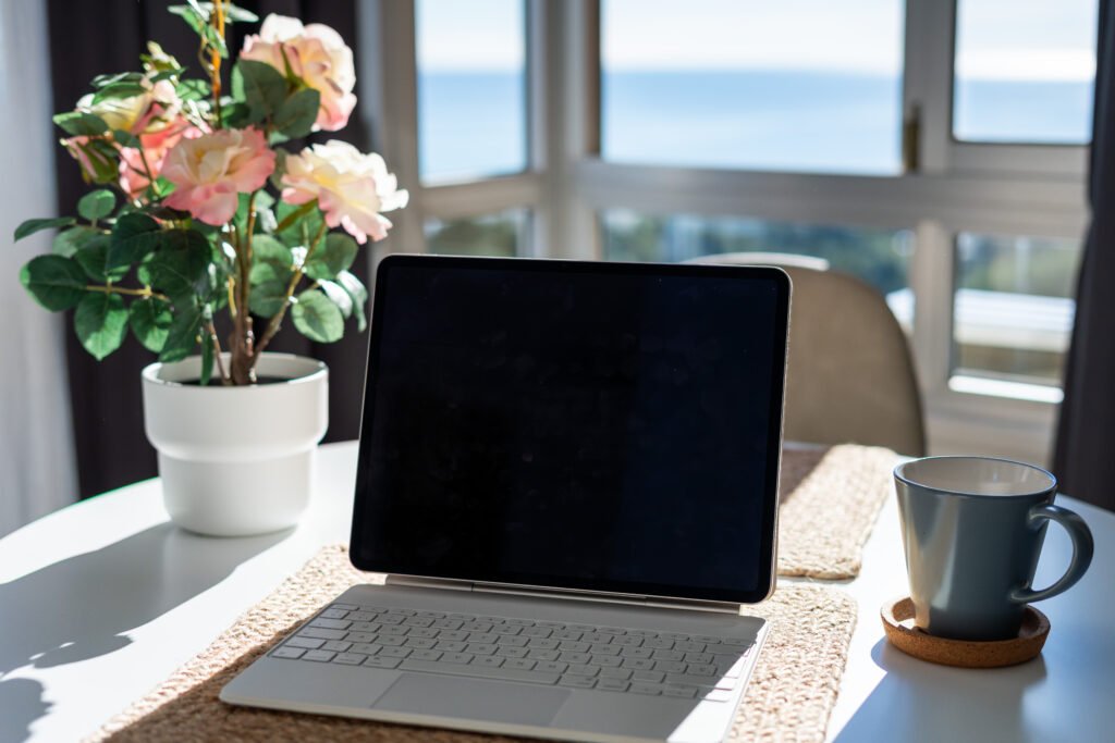Mesa con laptop, flores y taza.